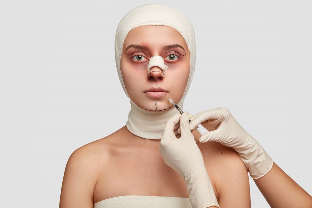 Image of doctor cosmetologist makes rejuvenation facial injection to patient does lip reduction procedure uses syringe. Woman in bandages recieves face treatment. Anti aging, plastic operation concept